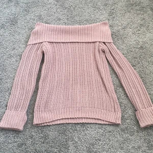 Rosa offshoulder stickad tröja - Säljer en jättefin stickad tröja i ljusrosa med offshoulder-modell. Tröjan har bred ribbad kant upptill och långa ärmar med uppvikta muddar. Perfekt för dig som vill ha en mysig men ändå trendig look.