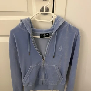 Ljusblå hoodie Juicy Couture - Supermjuk ljusblå hoodie från Juicy Couture i velour med dragkedja och huva. Ser helt ny ut bara att dragkedjans J har blivit pytte lite bronsig, men det är absolut inget som syns.