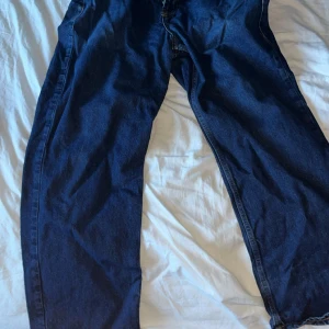 Mörkblå sweet sktbs jeans med gul text på bakfickor - Säljer ett par mörkblå jeans med loose fit och cool gul text i gotisk stil över bakfickorna. Jeansen har klassisk femficksdesign och raka ben. Perfekta för dig som vill sticka ut med en unik detalj på baksidan.