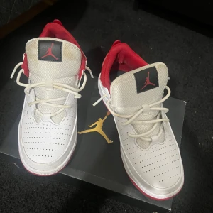 Vita och röda Nike Air Jordan sneakers - Säljer ett par fräscha Nike Air Jordan sneakers i vitt och rött. Skorna har perforerad tå, röda detaljer och klassisk Jumpman-logga på plösen. Ovandelen är i syntet och textil, med snörning och låg profil. Perfekta för dig som vill sticka ut med en ikonisk look.