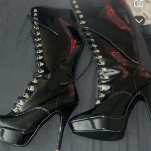 Svarta lackade platåstövletter med snörning - Höga svarta stövletter i glansigt lackmaterial med snörning hela vägen upp och rejäl platåsula. Vet inte riktigt storleken men kan gissa på 39or