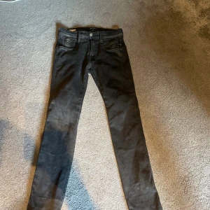 Svarta Replay Anbass slim jeans - Säljer ett par svarta Replay Anbass jeans i slim fit. Jeansen har klassisk femficksdesign, smal passform och är tillverkade i stretchigt jeansmaterial. Snyggt Replay-märke i linningen och diskret 'R' på bakfickan. Perfekta för en stilren look.
