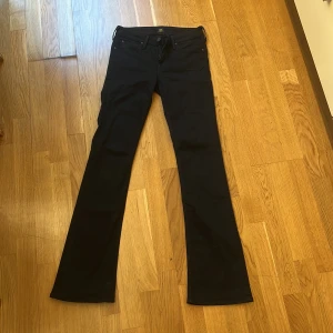 Svarta bootcut jeans från Lee W27 L33 - Snygga svarta jeans från Lee, modell Hoxie, med klassisk bootcut och low waisted. Jeansen har fem fickor, bälteshällor och Lee-logga bak. Materialet är mjukt för extra komfort. Perfekta för dig som gillar en tidlös look.