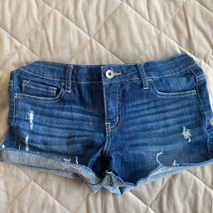 Blå jeansshorts från Klique B - Snygga blå jeansshorts från Klique B med slitna detaljer och upprullade benslut. Klassisk femficksmodell med knapp och dragkedja framtill. Perfekta för varma dagar och ger en avslappnad vibe.