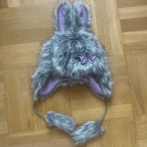 Pälsmössa med öron  - Söt grå pälsmössa med kaninöron och tofsar och en liten svans där bak!! Köpt i polen och säljs inte längre! För vuxna 💋 Liten lila rosett fram och lila foder i fleece. Unisex storlek  