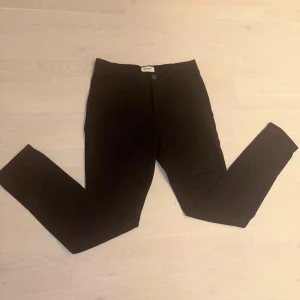Svarta chinos från Jack & Jones 31/34 - Snygga svarta chinos från Jack & Jones Pants Studio i storlek 31/34. Klassisk rak passform med knapp och dragkedja i midjan. Perfekta för en clean och stilren look. Tillverkade i mjukt bomullsmaterial för skön känsla hela dagen. Aldrig använda nypris 399