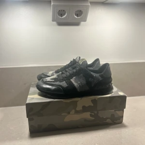 Valentino Rockrunner - Snygga Valentino Garavani Rockrunner sneakers i svart och grått med camouflage-mönster. Skorna har mesh och mockadetaljer, svarta snören och coola nitar på sulan. Perfekta för dig som vill sticka ut med exklusiva och trendiga sneakers.
