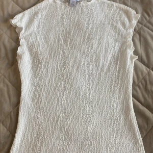 Vit strukturerad topp från Amisu XS - Säljer en vit topp från Amisu i storlek XS. Toppen har en strukturerad, vågig yta och är ärmlös med lätt fransiga kanter. Enkel och stilren modell som passar perfekt till jeans eller kjol.