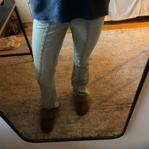 Ljusblå bootcut jeans med silver stenar (söm) - Säljer ett par ljusblå jeans med markerad söm längs benen(silver). Modellen har bootcut och sitter snyggt över höfterna. Jeansen har klassisk femficksdesign och dragkedja framtill. Perfekta för dig som gillar en retroinspirerad look.