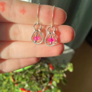 Silvriga örhängen med rosa pärlor - Unika örhängen i silverfärgad metall med droppformad design och en glittrande rosa pärla i mitten. Perfekt för dig som vill ha något färgstarkt och lekfullt i öronen. Lätta att bära och ger en snygg touch till din stil.