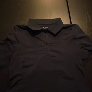 Marinblå pikétröja från Röhnisch S - Snygg marinblå pikétröja från Röhnisch i storlek S. Klassisk krage, tre knappar framtill och diskret logga på ärmen. Tröjan är tillverkad i ett mjukt och stretchigt material som känns skönt mot huden. Perfekt för en sportig och stilren look.