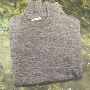  Zara tröja - En stilren grå stickad tröja från Zara med rund halsringning och långa ärmar. Tröjan är i mjukt material och har ribbade muddar vid ärmslut och nederkant. Perfekt för lager-på-lager och enkel att matcha med jeans eller chino och är bra till vintern 