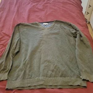 Randig grön tröja från Jack's V-ringad - Säljer en grön v-ringad tröja från Jack's i storlek XXL. Tröjan har tunna svarta ränder, ribbade muddar och är långärmad. Perfekt för dig som gillar en enkel men stilren look.