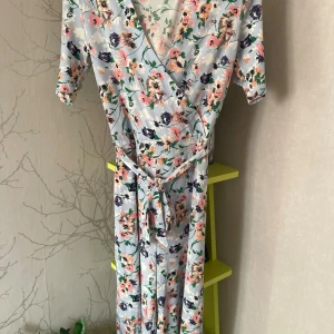 Blommig byxdress från Pieces - Superfin byxdress från Pieces i ljusblått med blommigt mönster i rosa, vitt, grönt och mörkblått. Omlottmodell med knytband i midjan och korta ärmar. Perfekt för sommarens alla tillfällen! Några noppror finns. 