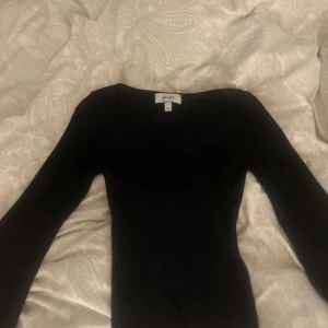 Svart ribbad stickad tröja AWARE - Svart långärmad stickad tröja från AWARE med ribbad struktur och snygg v-ringad halsringning. Tröjan har en figurnära passform och är perfekt för lager-på-lager under höst och vinter. Enkel men stilren design som funkar till allt.