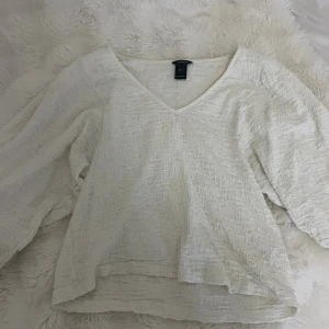 Vit blus med v-ringning från Lindex - Säljer en vit blus från Lindex i storlek S. Blusen har v-ringning, lång puffärm och är gjord i ett krinklat, strukturerat tyg som ger en cool och avslappnad känsla. Perfekt att styla med jeans eller kjol för en trendig look.