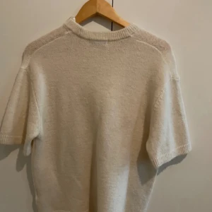 Beige stickad kortärmad tröja - En stilren beige stickad tröja med korta ärmar och rund hals. Tröjan har en mjuk och lite oversized passform, perfekt för lager på lager eller som den är. Enkel design som passar till det mesta.