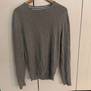 Grå basic tröja i bomull - En stilren grå tröja med rund halsringning och långa ärmar. Tröjan är i mjuk bomull och har en klassisk passform som funkar till allt. Perfekt för dig som gillar enkel och clean stil.