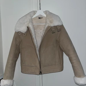 Beige teddyjacka från H&M med fuskpäls - Snygg beige teddyjacka från H&M med vit fuskpäls på krage och ärmslut och inuti hela jackan. Perfekt för kalla dagar. Ser ny ut utöver att det kommit lite smink vid kragen.🌸 