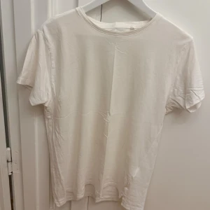 Vit t-shirt från WINWIN i bomull - Klassisk vit t-shirt från WINWIN i 100% ekologisk bomull. Enkel design med rund hals och korta ärmar, perfekt för en clean och avslappnad stil. Skön passform och mjukt material som känns bra mot huden. Storlek M.