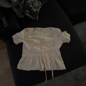 Ljusrosa blus från Zara Woman - Supersöt ljusrosa blus från Zara Woman med korta ärmar, knappar framtill och knytband i midjan. Blusen har en volangkant nedtill och en snygg, lite djupare rundad urringning. 