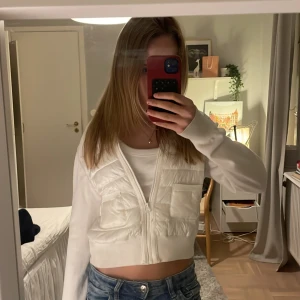 Vit croppad pufferjacka med dragkedja - Säljer en vit croppad pufferjacka med quiltad framsida och två fickor. Jackan har långärmade ribbade ärmar och dragkedja framtill. Perfekt för dig som gillar en clean och fräsch stil med lite edge. Liten i storlek så skulle säga att den passar 158-164 också. Pris kan diskuteras 💕kan ha några smink fläckar men kommer tvätta jackan innan någon köper🤗