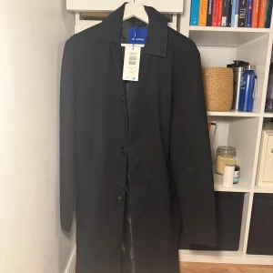 Svart rock från Jack & Jones - Stilren svart rock från Jack & Jones med klassisk krage och knäppning framtill. Lång modell med slät yta och diskret design, perfekt för dig som gillar en clean och tidlös look. Stor i storlek