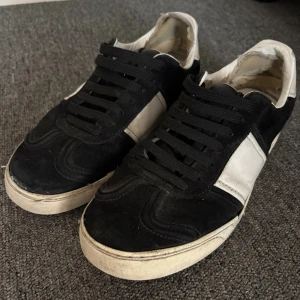 Valentino Rockstud svartvita sneakers - Svartvita Valentino Rockstud sneakers med klassiska nitar på hälen. Skorna har svart mocka och vitt skinn, rund tå och platt sula. Svarta snören och kontrasterande paneler ger en cool vibe. Perfekt för dig som gillar exklusiva detaljer och streetstyle. Det finns synliga defekter och skador och jag rekommendera att lämna in dessa på lagning. Därför ja säljer dessa billigt