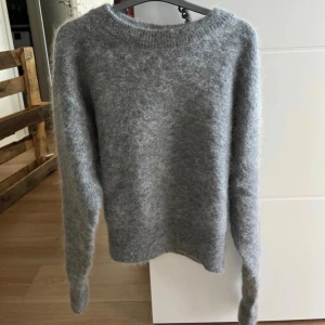 Grå fluffig mohair tröja - Supermjuk och fluffig grå stickad tröja med rund hals och långa ärmar. Perfekt för kyliga dagar och enkel att styla till jeans eller kjol. Tröjan har en klassisk passform och är riktigt cozy att dra på sig när det är kallt ute. Aldrig använd. 