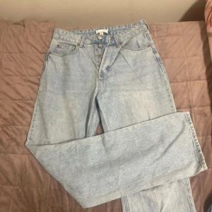 ljusblå jeans straight fit -  jeans i ljusblå denim med raka ben och hög midja. Byxorna har knappgylf och femficksdesign, tillverkade i bomull. Perfekta för en avslappnad och tidlös stil.