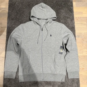 Grå Ralph lauren zip - Säljer nu denna riktigt feta Ralph lauren zip Hoodien i nyskick. Storlek M. Han på bild är 185cm, 74kg. Qr koden scannar till Ralph lauren hemsidan. Pris kan diskuteras vid snabb affär!