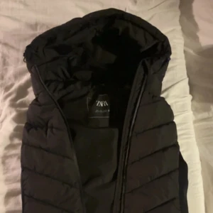 Svart dunväst med huva från Zara - Svart quiltad dunväst från Zara med huva och dragkedja. Har använt, de inte riktigt min styl nå mer