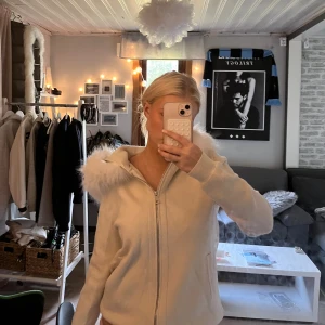 Vit hoodiejacka/kofta med fluffig huva - Säljer en vit kofta (kan användas som jacka) med dragkedja och stor fluffig huva med fejkpäls. Jackan har ribbade muddar vid nederkant samt fickor på sidorna. Koftan är köpt i en surfar butik i Spanien och har därför ingen lapp på sig men jag skulle säga att den lutar mot M/L hållet storleksmässigt. Säljer på grund av att jag knappast använder.