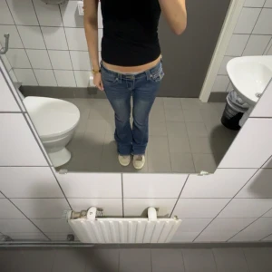 True Religion Joey Low Rise Flare Jeans - Säljer ett par blå True Religion Joey jeans med låg midja och flare-ben. Klassiska kontrastsömmar i gult, stora fickor med lock och snygga detaljer. Perfekt för dig som gillar 00-talsvibbar och vill sticka ut med ikoniska jeans.