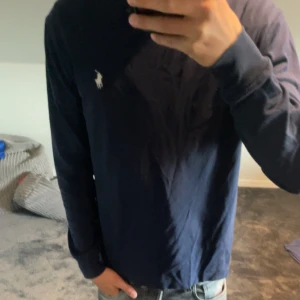 Mörkblå långärmad tröja Polo Ralph Lauren - Säljer en mörkblå långärmad tröja från Polo Ralph Lauren med klassisk vit broderad logga på bröstet. Tröjan är i mjuk bomull och har en normal passform, perfekt till jeans eller chinos. Enkel och stilren design med rund hals.