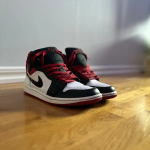 Nike Air Jordan 1 svart/vit/röd - Nike Air Jordan 1 sneakers med klassisk high-top siluett. Färgerna är svart, vit och röd med röda snören och svart swoosh. Skorna har rund tå, platt sula och är tillverkade i skinn. Perfekt för dig som gillar streetwear och ikoniska sneakers. Priset går att diskutera, bara att höra av sig👌🏼