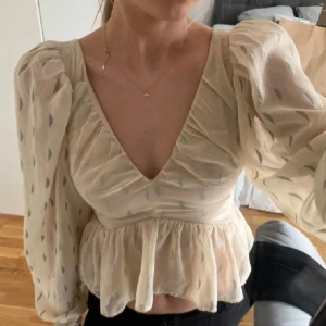 Beige blus med volang från H&M - Supersöt beige blus från H&M med silvriga detaljer och volang nertill. 