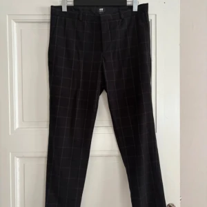 Svarta rutiga kostymbyxor H&M  - Svarta kostymbyxor från H&M i skinny fit med diskret rutmönster. Byxorna har hällor för bälte, knapp- och dragkedjestängning samt bakfickor med knappar. Perfekta för en clean och stilren look.