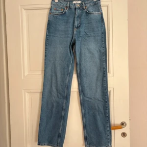 High waist straight jeans från NA-KD - Blå high waist straight jeans från NA-KD i klassisk denim med fem fickor och orangea sömmar. Jeansen har en rak passform och stängs med dragkedja och knapp framtill. Perfekta för en avslappnad och trendig look.