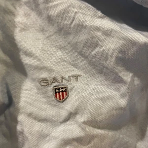 Ljusblå skjorta från Gant - Klassisk ljusblå skjorta från Gant med broderad logga på bröstet. Skjortan har långa ärmar, knappar framtill och är tillverkad i mjuk bomull. Perfekt för en clean och stilren look. Behöver strykas annars mycket fint skick!! Barnsstorlek men passar man som bär S.
