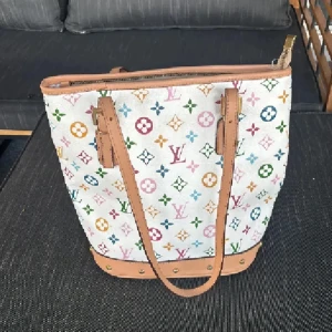  multicolor axelväska - Snygg axelväska  i vitt med ikoniskt multicolor-mönster och klassiska loggor i olika färger. Väskan har ljusbruna skinnhandtag, detaljer i guld och dragkedja upptill. Perfekt storlek för att få plats med allt du behöver.