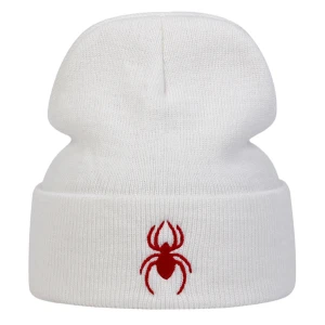 Vit mössa med röd spindelbrodyr - Vit ribbstickad mössa med uppvikt kant och en broderad röd spindel framtill. Mössan har en klassisk form och är tillverkad i mjukt stickat material som håller dig varm och ger en clean look med en edgy detalj.