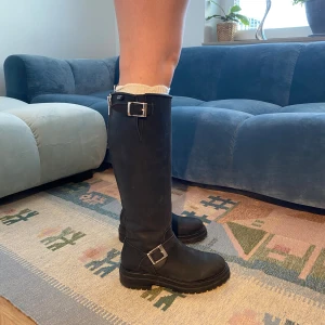 Limited edition Johnny Bulls Svarta höga boots med spännen - Säljer ett par svarta höga boots med rejäl sula med paladium spännen. Stövlarna är i läder och har rund tå samt dragkedja på baksidan. Perfekta för dig som vill ha en edgy, stilren look till höst och vinter. Knappt använda. 