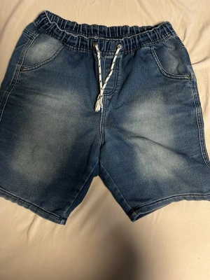 Blå jeansshorts med snörning Pepperts - Säljer ett par blå jeansshorts från Pepperts i storlek 164. Shortsen har elastisk midja med vit snörning, två fickor fram och två bakfickor med dekorativ söm. Materialet är mjuk denim och passformen är loose för en avslappnad stil.