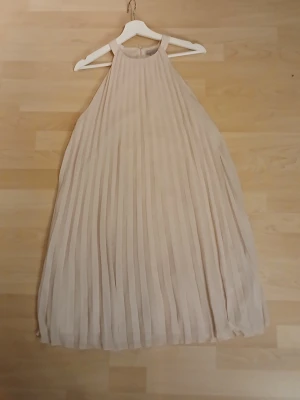 Beige plisserad långklänning H&M - Säljer en elegant beige långklänning från H&M i plisserad polyester. Klänningen har ärmlös design med breda axelband och ett luftigt fall. Perfekt för dig som gillar stilrena och ljusa toner. Materialet är 100% polyester och modellen är riktigt flowy.