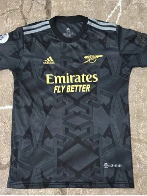 Arsenal x Adidas svart matchtröja - Säljer en svart Arsenal matchtröja från Adidas med gul logga och tryck. Tröjan har ett geometriskt mönster över hela ytan och grå ränder på axlarna. Perfekt för fotbollsfans som vill ha en snygg och bekväm tröja med Aeroready-material.