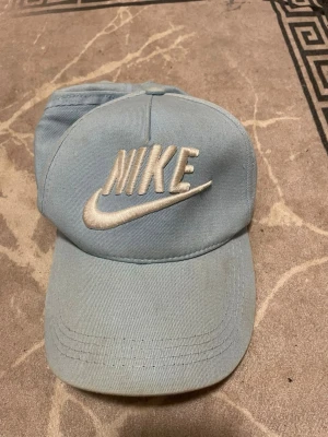 Ljusblå Nike keps med broderad logga - Säljer en ljusblå keps från Nike med stor broderad logga i vitt framtill. Kepsen har klassisk böjd skärm och justerbart band bak för perfekt passform. Tillverkad i bomullstyg som känns skönt och andas. Perfekt accessoar för en sportig och avslappnad stil.