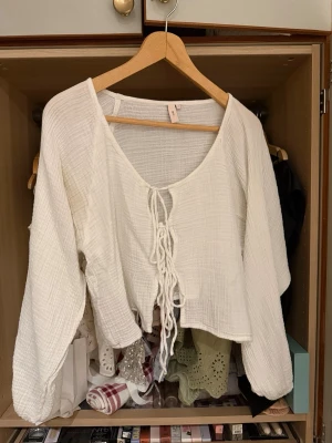 Vit blus med snörning från Nelly - Säljer en luftig vit blus från Nelly i storlek S. Toppen har vida ärmar, croppad passform och snygg snörning framtill. Tillverkad i ett mjukt bomullsliknande material med lätt struktur. Perfekt för sommarens alla tillfällen!