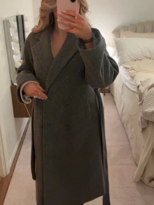 Kappa - Lång grå kappa med fickor, slits i bak, knappar och ett band att knyta i storlek xs från lager 157