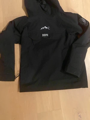 Svart skid/snowjacka från Dope Snow XS - Svart vindjacka från Dope Snow i storlek XS. Jackan har huva, stor ficka framtill med logotyp, och tryck på ärmen. Materialet är slitstark polyester och passformen är loose. Perfekt för dig som gillar streetwear och vill ha en snygg jacka med grymma detaljer. Har bara använts en gång, originala priset är 2000kr. Kan skicka mer bilder på jackan privat och priset kan diskuteras 💓